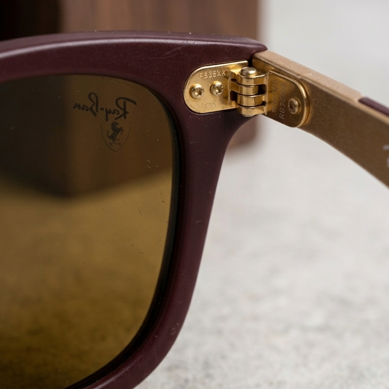 Close-up of a maroon sunglasses with gold hinges on a textured surface.